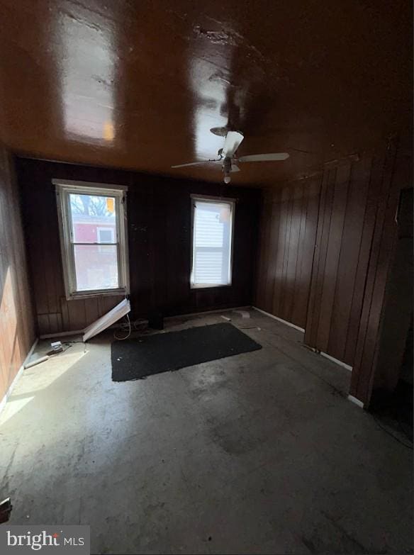 empty room featuring a healthy amount of sunlight, wooden walls, and concrete flooring