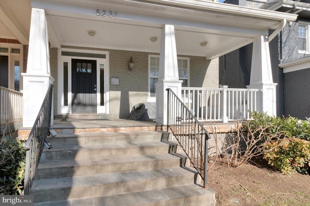 entrance to property featuring a porch and brick siding