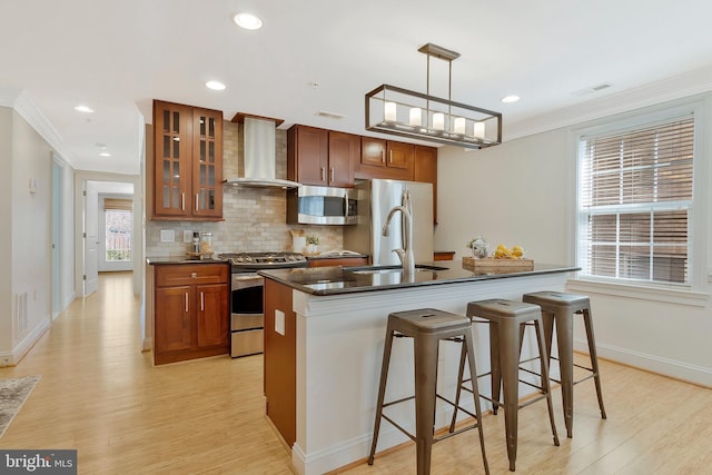 kitchen featuring a sink, appliances with stainless steel finishes, wall chimney range hood, dark countertops, and crown molding