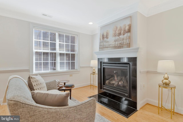 living area with visible vents, ornamental molding, a glass covered fireplace, wood finished floors, and baseboards