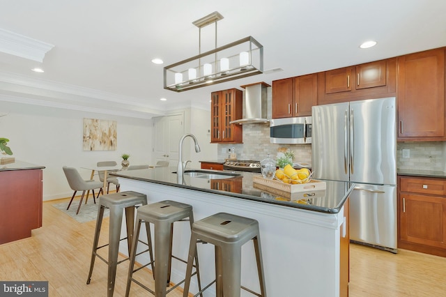 kitchen featuring light wood finished floors, dark countertops, appliances with stainless steel finishes, wall chimney range hood, and a sink