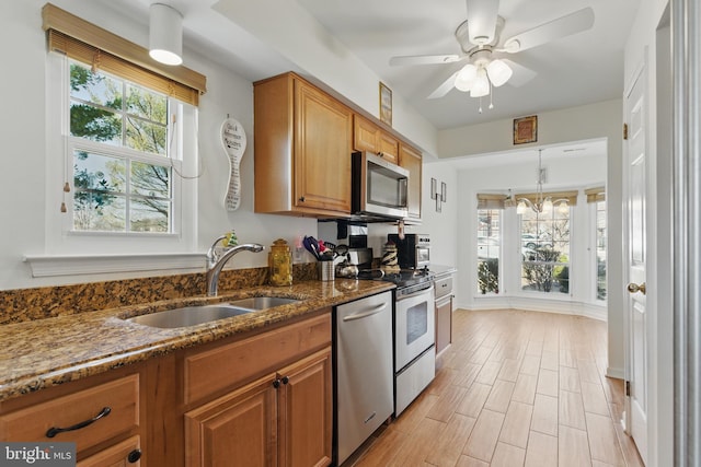 kitchen with light wood-type flooring, dark stone countertops, appliances with stainless steel finishes, brown cabinetry, and a sink