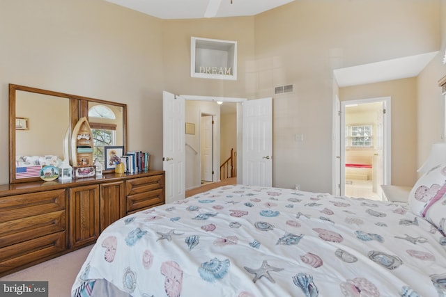 carpeted bedroom with visible vents, multiple windows, high vaulted ceiling, and ensuite bath