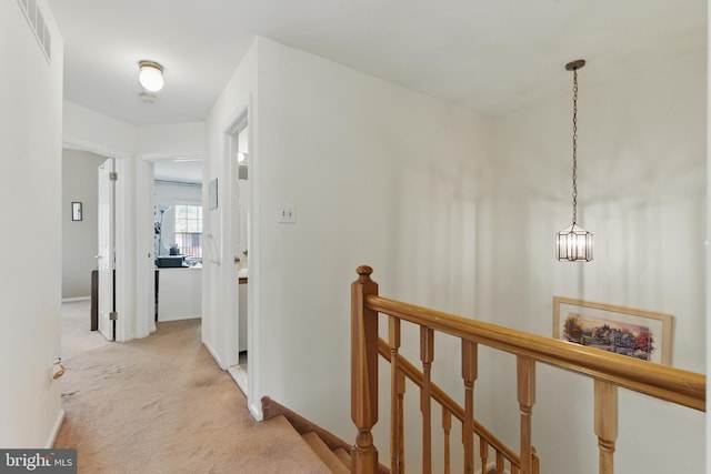 hallway featuring an upstairs landing, visible vents, light colored carpet, and baseboards