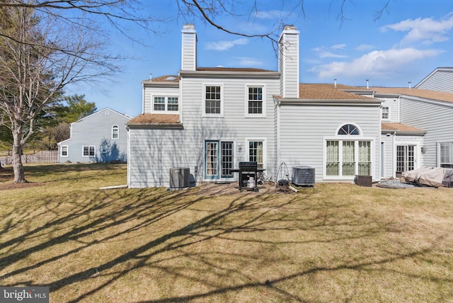 rear view of property with a lawn, central AC, a chimney, and roof with shingles