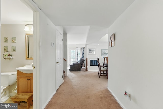 hall featuring a sink, baseboards, and light carpet