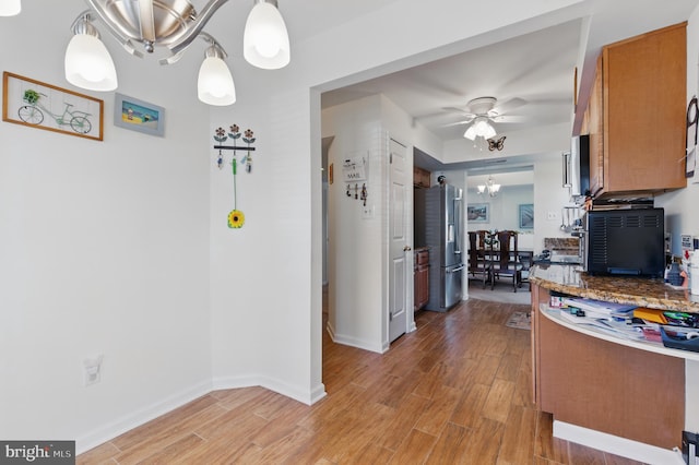 kitchen featuring baseboards, light wood-style flooring, ceiling fan with notable chandelier, brown cabinets, and stainless steel refrigerator with ice dispenser