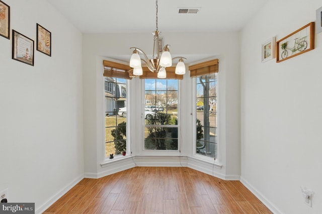 unfurnished dining area featuring visible vents, baseboards, a notable chandelier, and wood finished floors