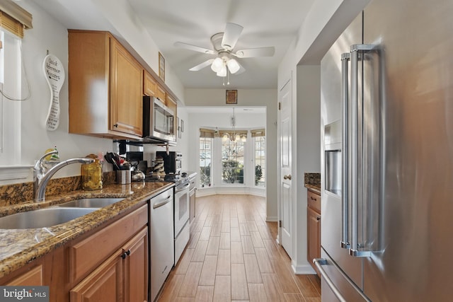 kitchen featuring brown cabinetry, wood finish floors, dark stone counters, a sink, and stainless steel appliances