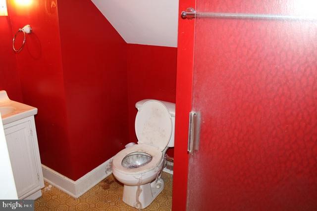 half bath featuring lofted ceiling, baseboards, toilet, and vanity