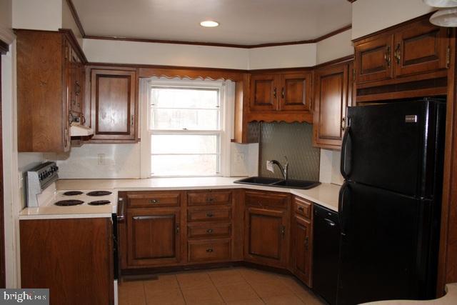 kitchen with black appliances, ornamental molding, light countertops, and a sink