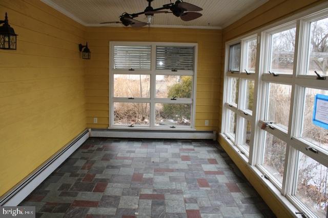 unfurnished sunroom with baseboard heating, a ceiling fan, and a healthy amount of sunlight