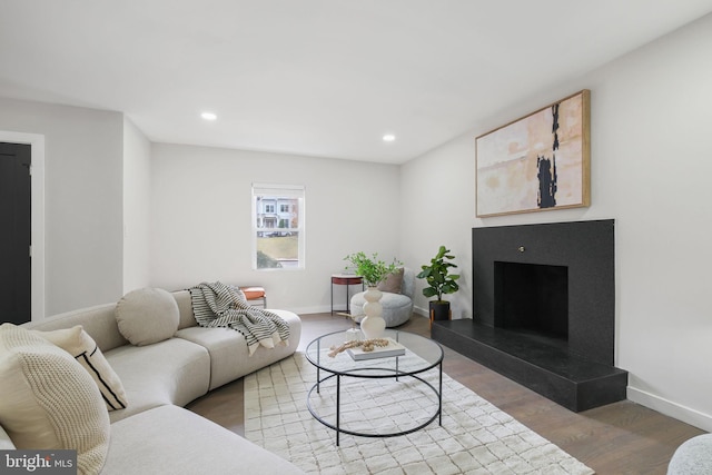 living area featuring recessed lighting, a fireplace with raised hearth, baseboards, and wood finished floors