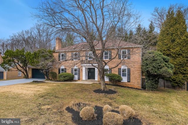 colonial home with concrete driveway, a chimney, fence, a front yard, and brick siding