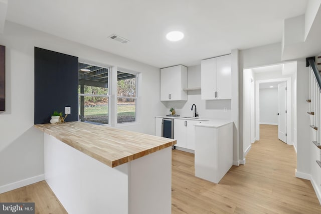 kitchen with light wood-style flooring, a peninsula, wood counters, visible vents, and white cabinetry