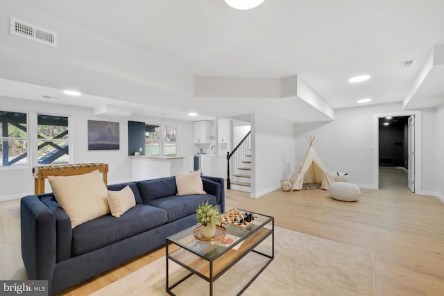 living area with stairs, baseboards, visible vents, and light wood-style floors