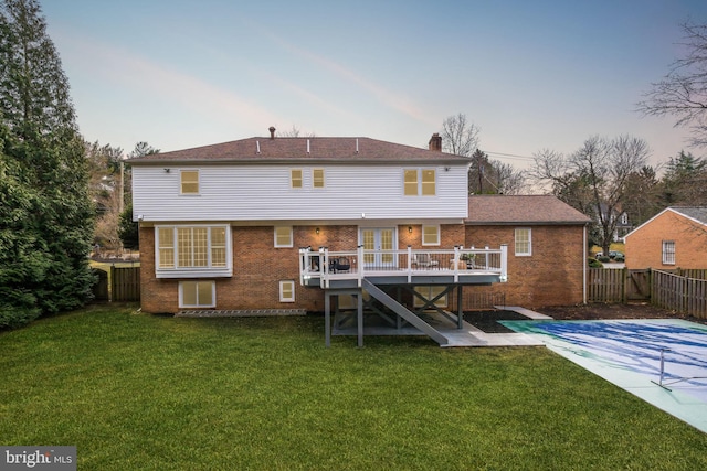 rear view of house with a fenced backyard, a deck, a lawn, and brick siding