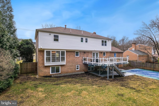 rear view of house with a fenced backyard, a lawn, a deck, and brick siding