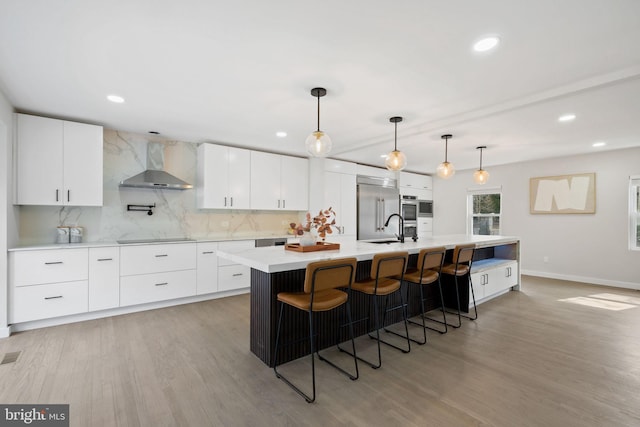 kitchen with light wood-style flooring, decorative backsplash, stainless steel built in fridge, modern cabinets, and wall chimney exhaust hood