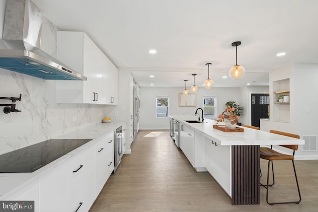 kitchen with black electric stovetop, visible vents, white cabinets, a sink, and wall chimney exhaust hood