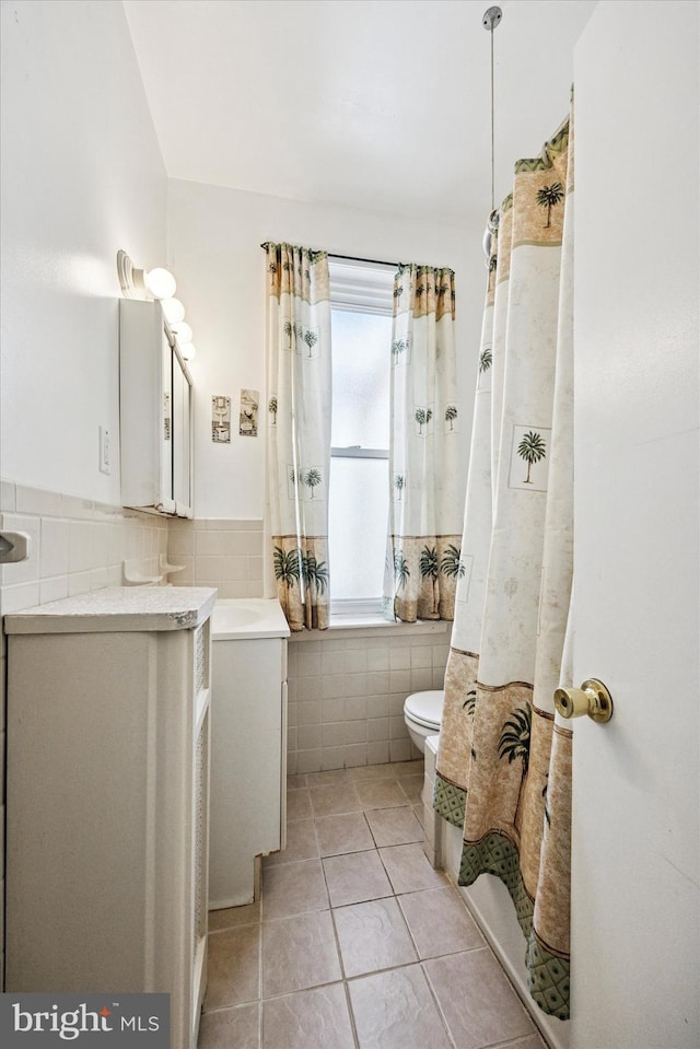 bathroom featuring a wainscoted wall, tile walls, toilet, vanity, and tile patterned flooring