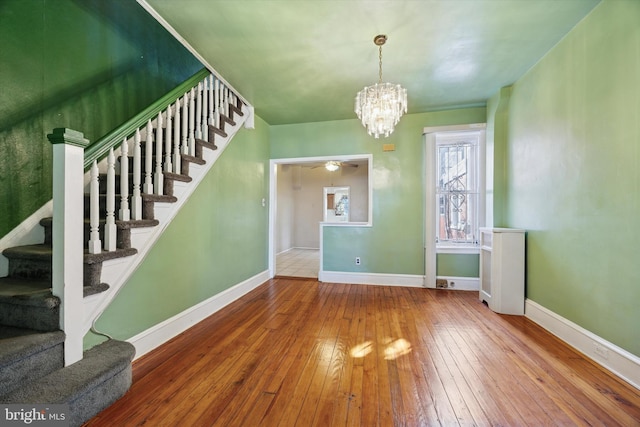 unfurnished dining area featuring ceiling fan with notable chandelier, wood-type flooring, baseboards, and stairs