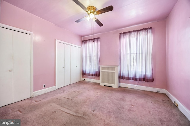 unfurnished bedroom featuring baseboards, a ceiling fan, radiator heating unit, carpet flooring, and multiple closets