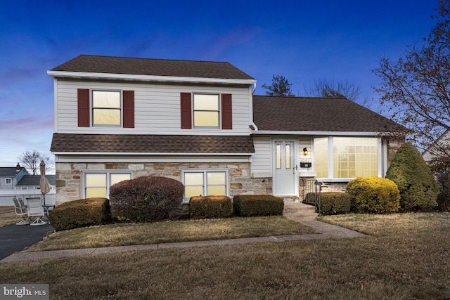 split level home with stone siding, a shingled roof, and a front yard