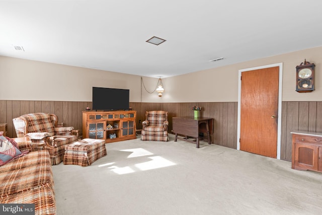 carpeted living room featuring wooden walls, wainscoting, and visible vents