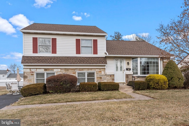 split level home with stone siding, a front lawn, and roof with shingles