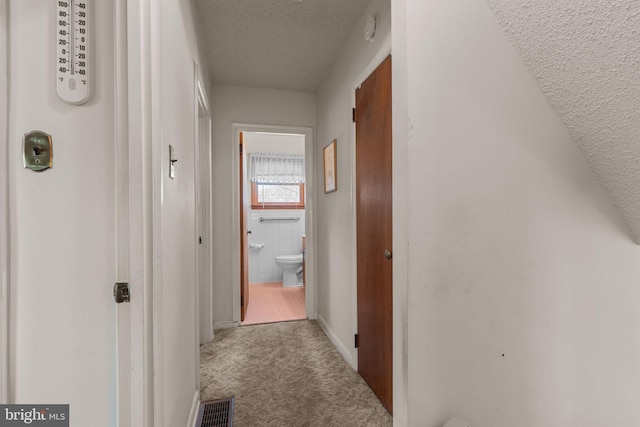 corridor featuring a textured ceiling, carpet, visible vents, and tile walls