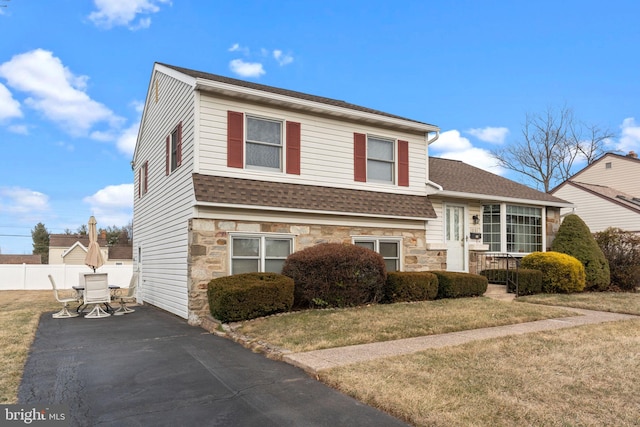 tri-level home featuring a shingled roof, stone siding, fence, and driveway