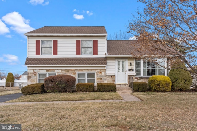 split level home with stone siding, a shingled roof, and a front yard