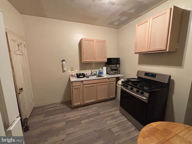 kitchen with wood finished floors, a sink, baseboards, light countertops, and gas stove