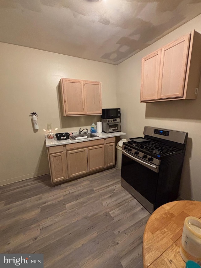 kitchen featuring a sink, baseboards, light countertops, dark wood-style floors, and gas range