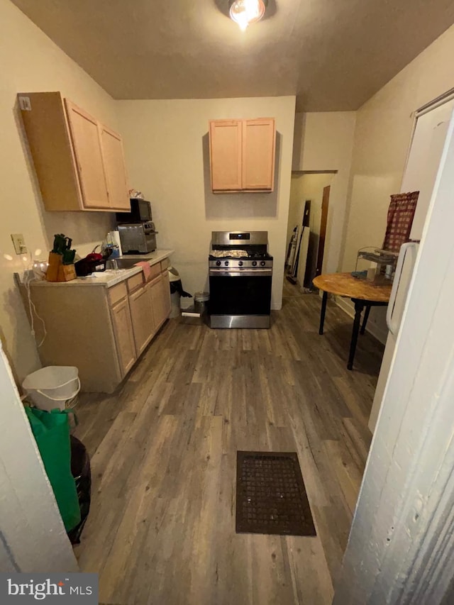 kitchen with light countertops, light brown cabinetry, dark wood-style flooring, and gas stove