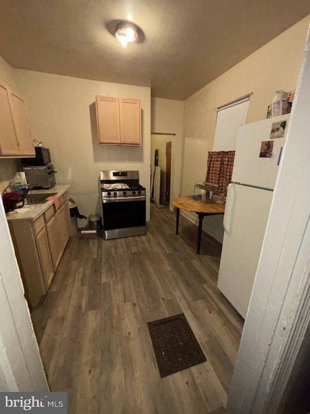 kitchen featuring freestanding refrigerator, dark wood-style flooring, light countertops, and stainless steel gas range oven