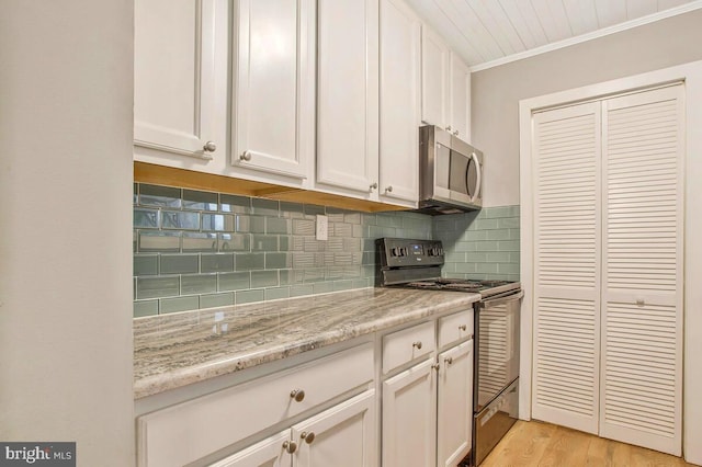 kitchen with black range, white cabinets, decorative backsplash, light wood finished floors, and stainless steel microwave