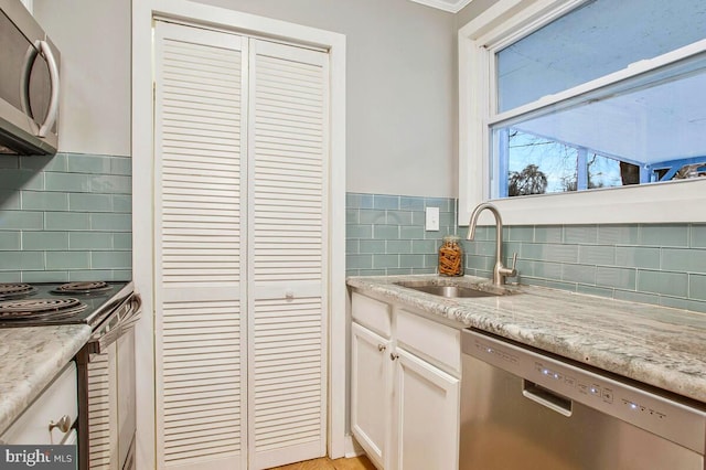 kitchen featuring tasteful backsplash, white cabinets, light stone countertops, stainless steel appliances, and a sink