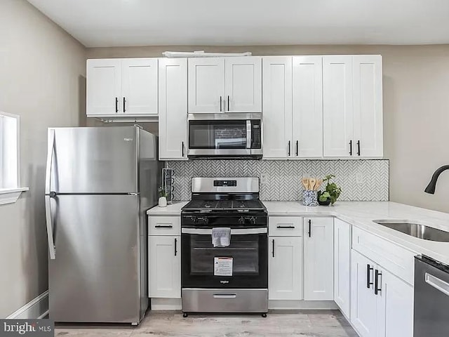 kitchen featuring decorative backsplash, appliances with stainless steel finishes, light countertops, white cabinetry, and a sink