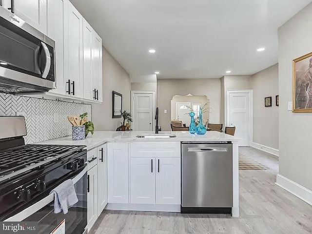 kitchen featuring a peninsula, appliances with stainless steel finishes, a sink, and white cabinetry