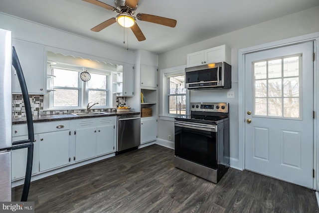 kitchen with dark wood finished floors, dark countertops, stainless steel appliances, open shelves, and a sink