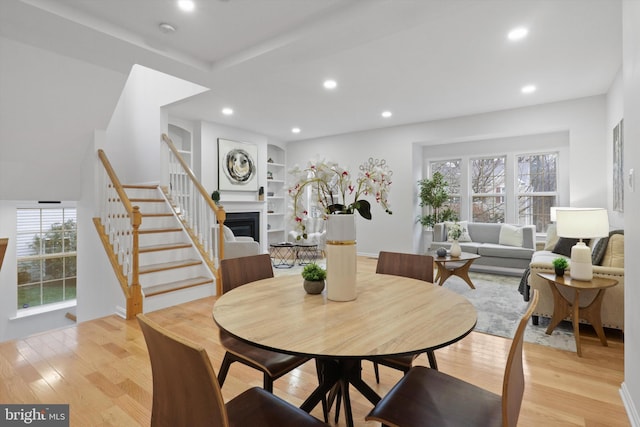 dining area featuring built in features, light wood-style flooring, recessed lighting, stairs, and a glass covered fireplace