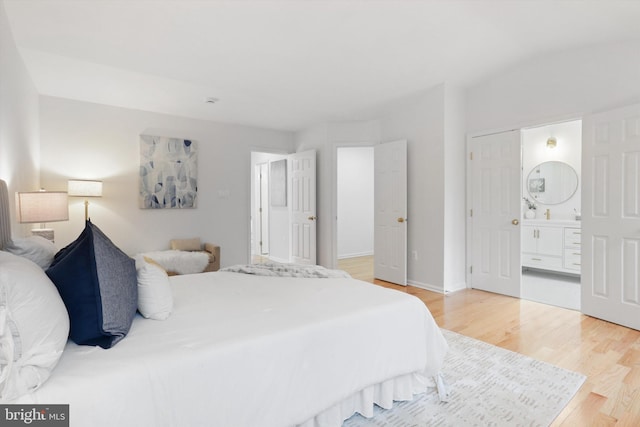 bedroom with baseboards, ensuite bath, and light wood-style flooring