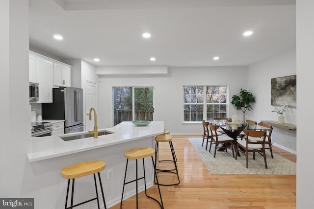 kitchen with a kitchen bar, light wood-style flooring, a sink, white cabinetry, and stainless steel appliances