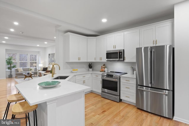 kitchen with open floor plan, appliances with stainless steel finishes, a peninsula, white cabinetry, and a sink