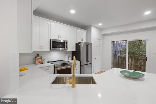 kitchen featuring backsplash, light stone countertops, appliances with stainless steel finishes, white cabinets, and a sink