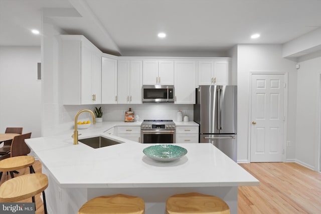 kitchen featuring a breakfast bar, a peninsula, white cabinets, stainless steel appliances, and a sink