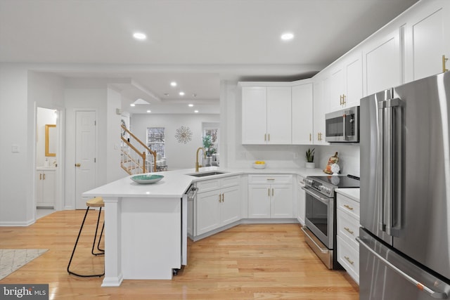 kitchen with light wood finished floors, appliances with stainless steel finishes, a peninsula, white cabinetry, and a sink