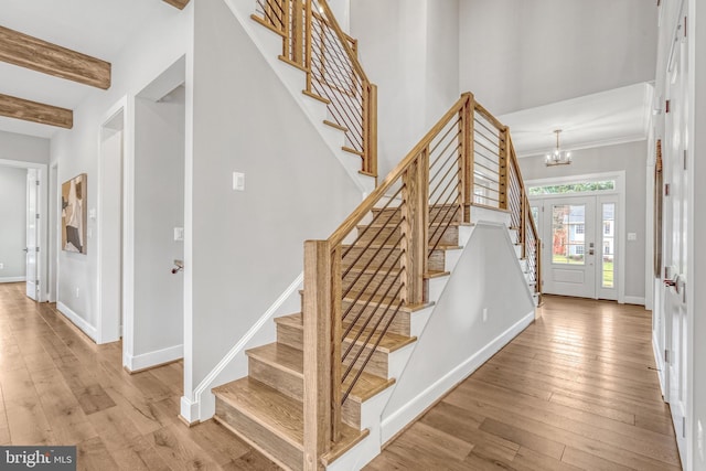 stairway featuring a chandelier, beamed ceiling, hardwood / wood-style flooring, and baseboards